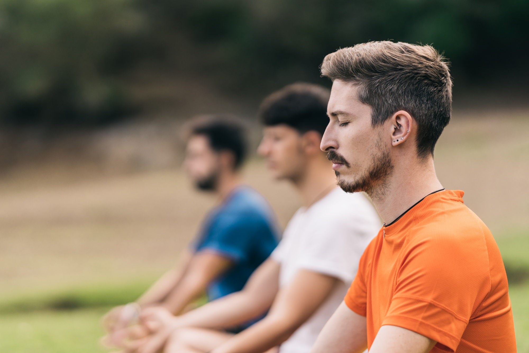 Three men practising the yoga lotus position in a park
